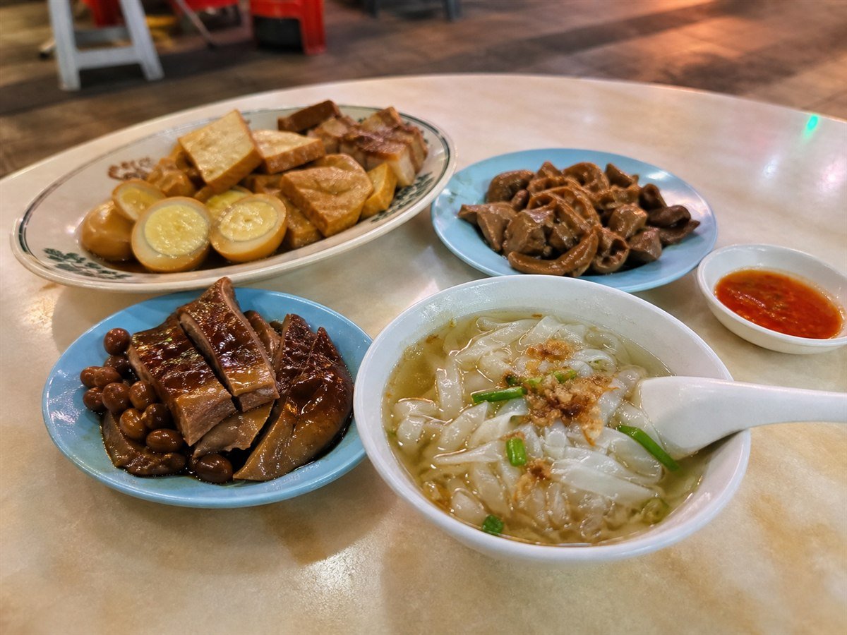 Kway teow kia with clear rice-noodle soup and plates of soy-braised meats, tofu and egg