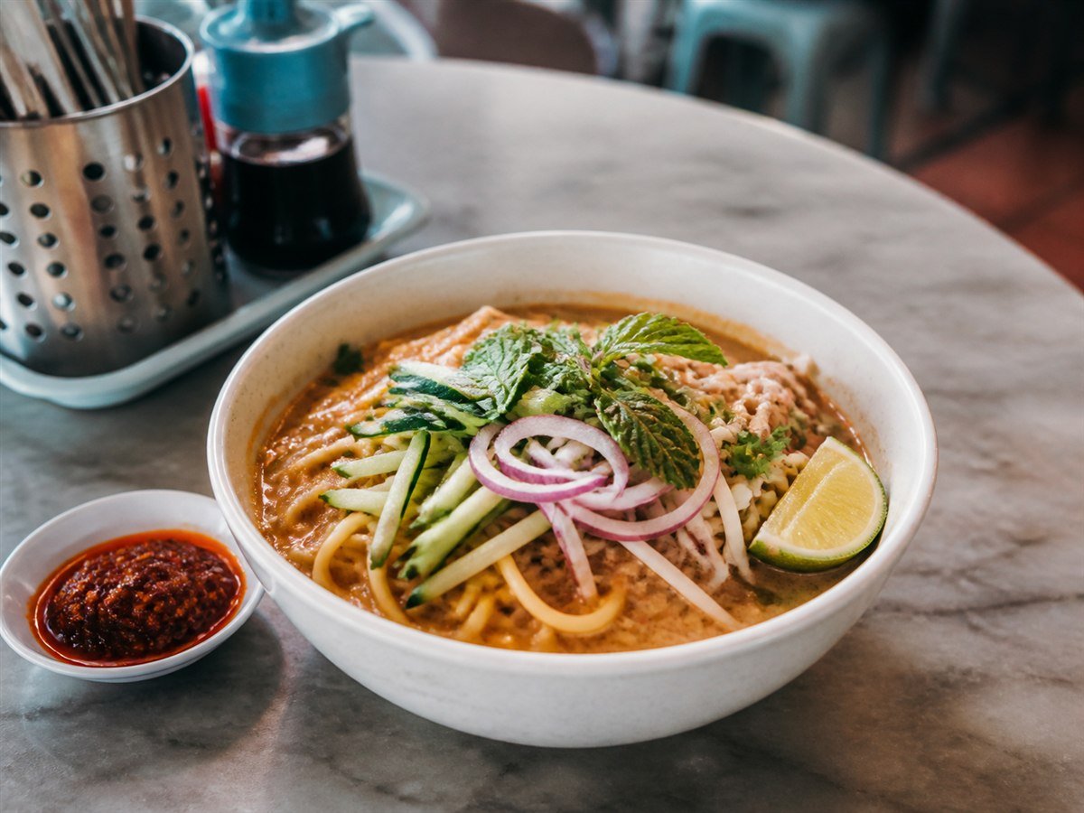A bowl of Laksa Johor with spaghetti, fish gravy, fresh herbs and sambal
